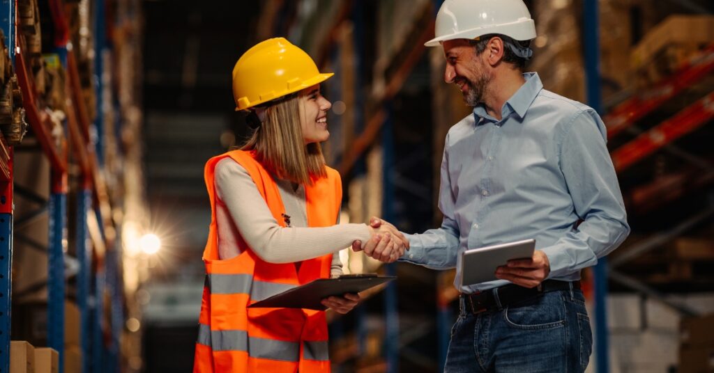 worker in protective work wear shaking hands in a large warehouse