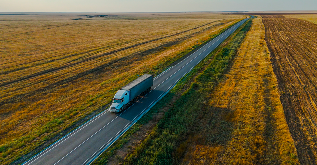 An aerial shot of a white semi-truck driving along a two-lane highway.