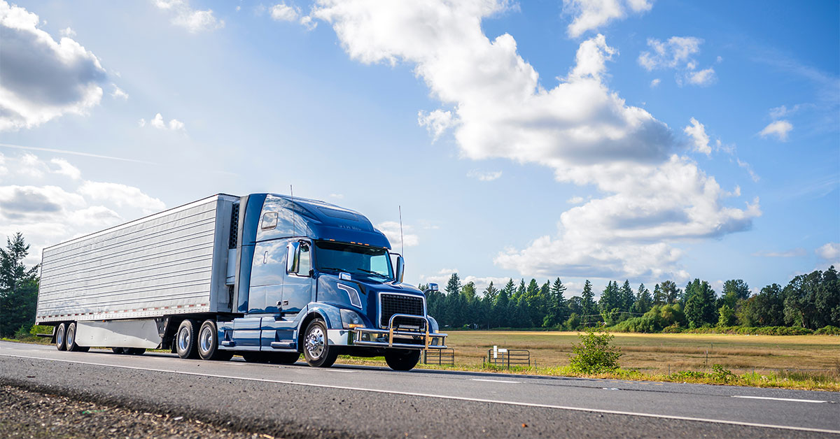 a blue semi truck and white trailer driving down the highway