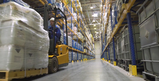 man with pallets on a machine in warehouse aisle