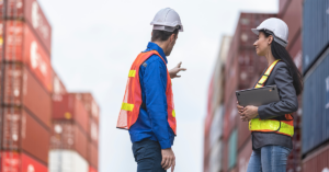 two people having a discussion while standing next to shipping containers