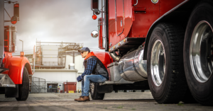 A truck driver sitting on the side step of a red semi-truck