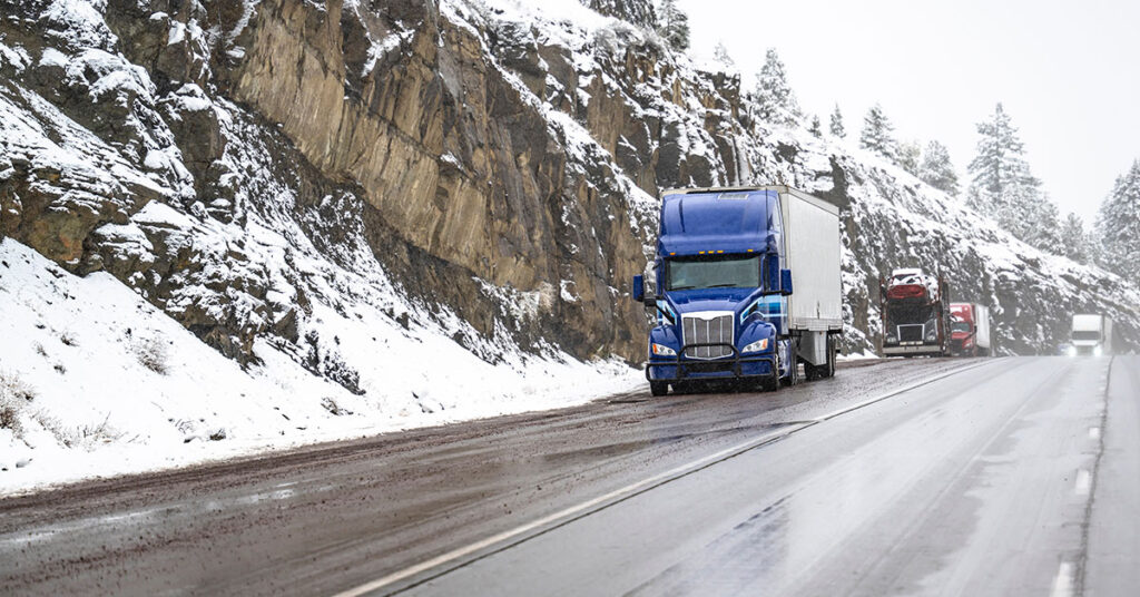 Semi truck and trailers driving on a wet road surrounded by snow