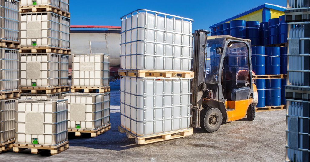 Forklift moving stacked IBC tote tanks in an industrial yard.