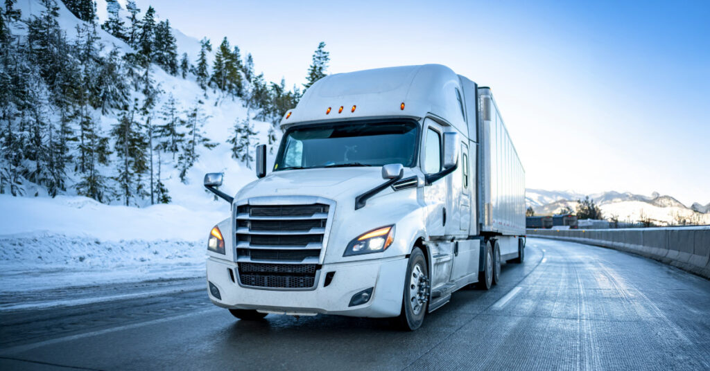 A semi trailer driving on the road surrounded by snow