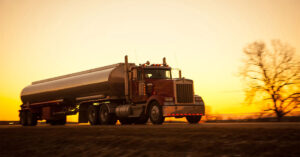 A tanker truck driving down the road with the sunset in the background