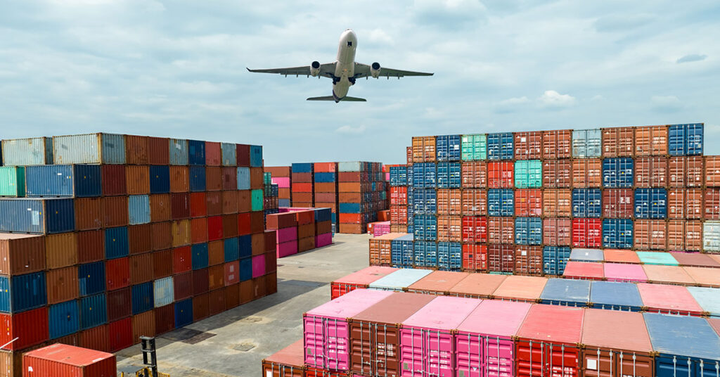an airplane flying over cargo containers within a shipping port