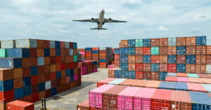 an airplane flying over cargo containers within a shipping port