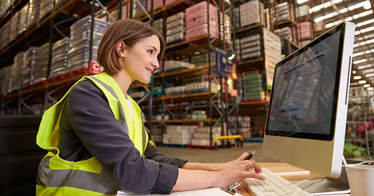 a woman typing on a keyboard and looking at a computer in a warehouse