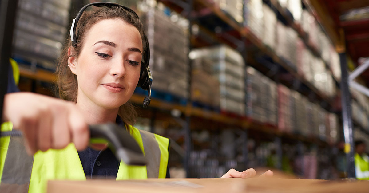 a woman wearing a safety vest scanning a box in a warehouse