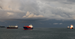 Four cargo ships stationed in the water as the sky is filled with dark storm clouds.